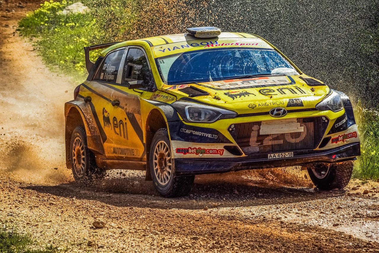 Yellow rally car driving towards the right on a dirt track